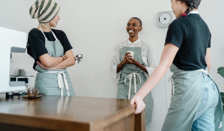 Minijob-Erhöhung auf 600 Euro: ab wann gilt der neue Satz? Minijob 600 Euro, fröhliche Mitarbeiterin in Schürze im Café an der Theke