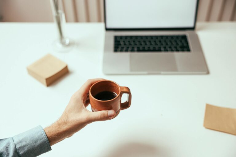 Mittwoch Sprüche – Person hält eine Tasse Kaffee neben dem Laptop im Büro