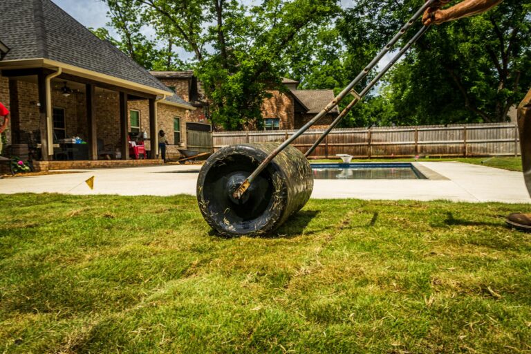 Rasenwalze selber bauen, Arbeiter walzt einen Rasen im Vorgarten an einem sonnigen Tag