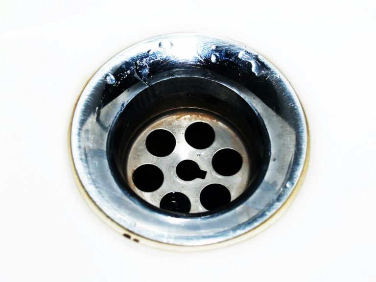 Schwarze Würmer im Abfluss: was hilft wirklich? Schwarze Würmer im Abfluss, Nahaufnahme eines Chrom-Abflusses mit Wassertropfen